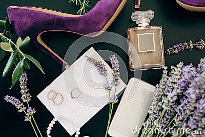 Lilac high heel shoe, a bottle of perfume, a smartphone, jewelry and flowers on a green background Stock Photo