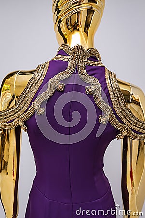 Long, lilac designer, evening, women`s dress handmade on gold, glossy mannequin. With white and gold bead ornament. Isolated on gr Stock Photo