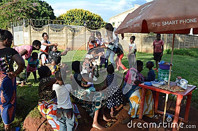 LILONGWE, MALAWI, AFRICA - APRIL 2, 2018: Bright road scene, african women and children are sitting along the roads, smiling and Editorial Stock Photo