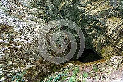 Limestone cliff wall with entrance of the cave. Cave in a layered limestone rock Stock Photo