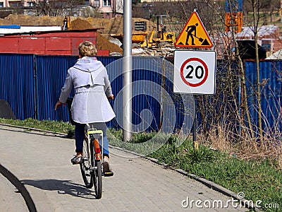 Limitation of traffic to 20 km/h near the construction site. A woman on a bicycle is driving along the sidewalk near the construct Editorial Stock Photo