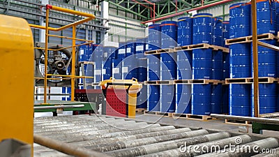 Line production used for filling chemicals into 200 liter drums. Blue barrel chemical drums are stacked on wooden pallets inside Stock Photo