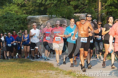 A line of runners racing a crowded 5K in a park on a summer evening Editorial Stock Photo