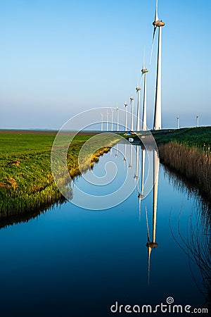 Line of windmills reflecting on a channel of water Stock Photo