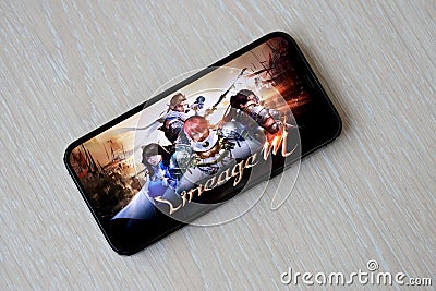 Lineage M mobile iOS game on iPhone 15 smartphone screen on wooden table during mobile gameplay Editorial Stock Photo