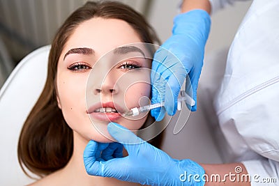 Lip Augmentation. Closeup Of Beautician Doctor Hands Doing Beauty Procedure To Female Lips with Syringe. Young Woman`s Stock Photo