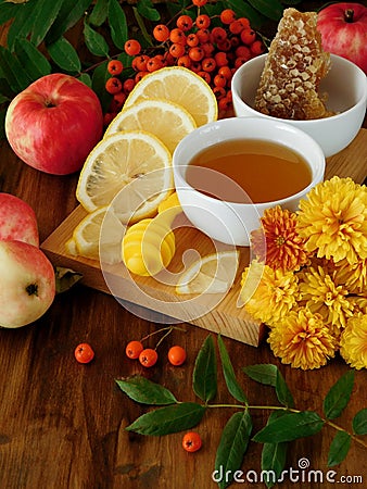 Liquid honey in a little bowl surrounded by slices of lemon, apples, rowan berries and flowers Stock Photo