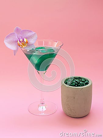 Liquid spirulina green drink with Phalaenopsis in cocktail glass and spirulina pills on pink background. Stock Photo