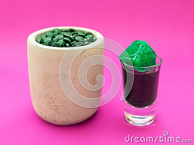 Liquid spirulina green drink in short cocktail glass and spirulina pills on pink background. Stock Photo