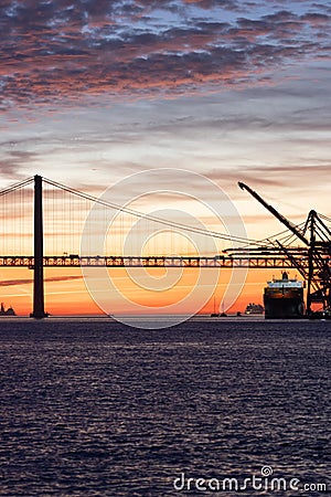 Lisbon 25th of April Bridge at sunset and industrial working cranes Stock Photo