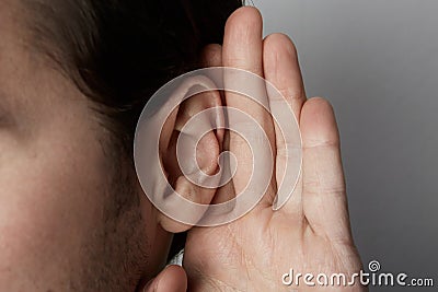 Listening male holds his hand near his ear over grey background.Closeup. Stock Photo