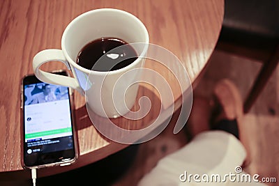 Listening to music on a smartphone while drinking coffee alone in a cafe Stock Photo