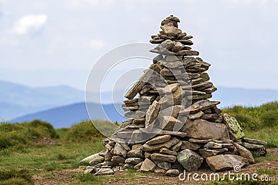 Lit by bright summer sun uneven mountain stones stacked and balanced like pyramid pile on green grassy valley on light white blue Stock Photo