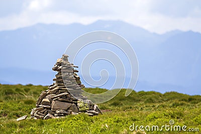 Lit by bright summer sun uneven mountain stones stacked and balanced like pyramid pile on green grassy valley on light white blue Stock Photo