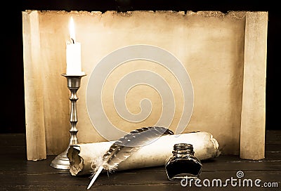 A lit candle and quill with inkwell against a background of a scroll of parchment Stock Photo