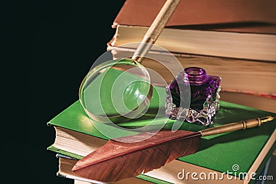 Literature concept. Inkstand with feather near magnifying glass on old books against black background Stock Photo