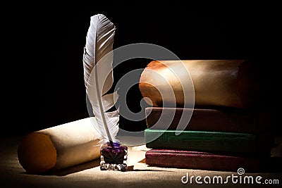 Literature concept. Old inkstand with feather near scrolls and books against black background. Dramatic light Stock Photo