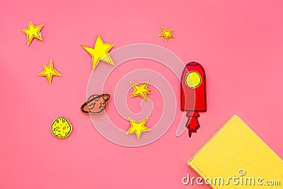 Literature about cosmos for school children. Book with blank cover near cutout of rocket, stars, moon on pink background Stock Photo