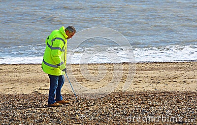 Litter picking on Felixstowe Beach by man in yellow jacket. Editorial Stock Photo
