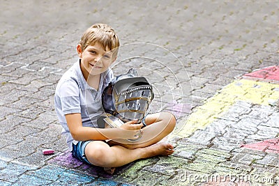 Little active kid boy drawing knight castle and fortress with colorful chalks on asphalt. Happy child with big helmet Stock Photo