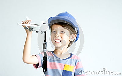 Little adorable Caucasian boy wearing hard hat, standing on white background, holding and playing airplane toy, smiling with Stock Photo