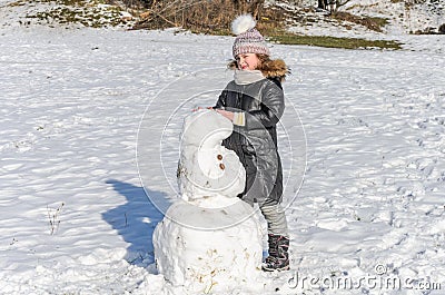 Little adorable girl child sculpts snowman from snow in winter Stock Photo