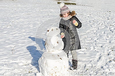 Little adorable girl child sculpts snowman from snow in winter Stock Photo