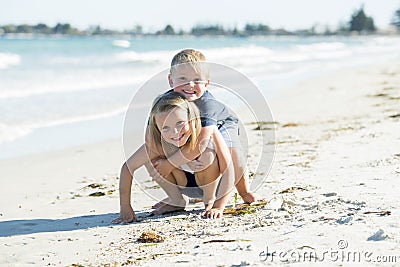 Little adorable and sweet siblings playing together in sand beach with small brother hugging his beautiful blond young sister enjo Stock Photo