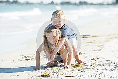 Little adorable and sweet siblings playing together in sand beach with small brother hugging his beautiful blond young sister enjo Stock Photo