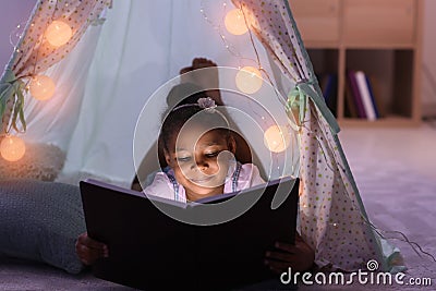 Little African-American girl reading bedtime story in hovel Stock Photo