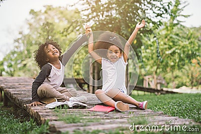 Little Afro child girl reading book between green spikes meadow garden with friend Stock Photo