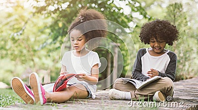 Little Afro child girl reading book between green spikes meadow garden with friend Stock Photo