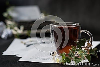 Little alien sits on paper with text near a cup of tea and green ivy leaves. Typewriter with a sheet of paper. Crumpled paper. Stock Photo