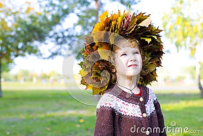 Little amusing girl in a wreath from autumn leaves Stock Photo