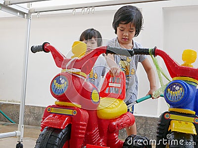 Little Asian baby girl learning to wash plastic big bikes while her little sister watching and standing nearby Stock Photo