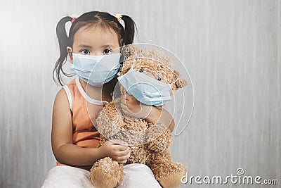 Little asian girl child holding a teddy bear wearing a mask. Stock Photo