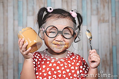 Little asian girl holding and enjoying peanut butter in jar and a spoon Stock Photo