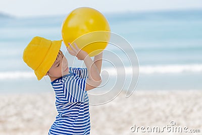 Little asian girl playing yellow ball on the beach in summer. Little girl have enjoy and happy. Stock Photo