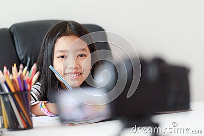 Little Asian girl sitting at the white table and live streaming for social media by camera select focus Stock Photo