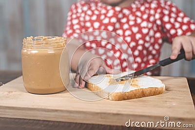 Little asian girl spreading a peanut butter on a white bread. Stock Photo
