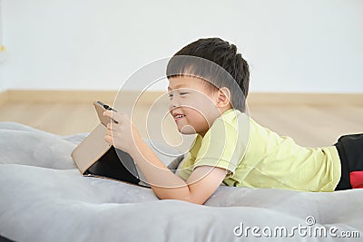 Little Asian kindergarten boy child lying on his stomach while using tablet pc, Gadget addicted kid Stock Photo