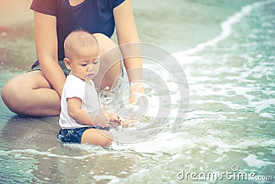 Little Asian 10 months baby excited playing the beach first time. Mother closely take care baby while playing the water Stock Photo