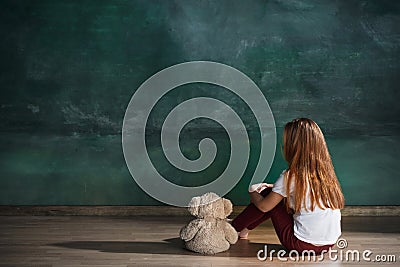 Little girl with teddy bear sitting on floor in empty room. Autism concept Stock Photo