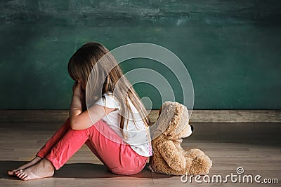 Little girl with teddy bear sitting on floor in empty room. Autism concept Stock Photo