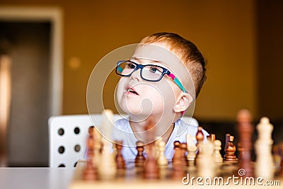 Little baby boy with down syndrome with big blue glasses playing chess in kindergarten Stock Photo