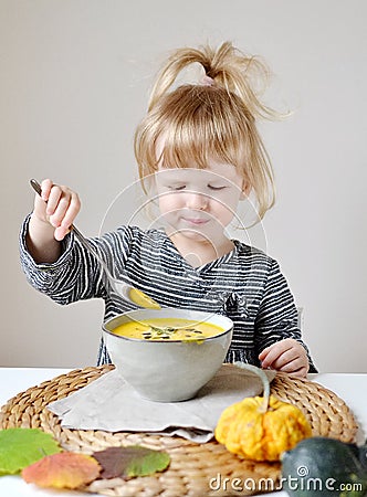 Little Girl Eating Pumpkin Cream-Soup at Home Stock Photo