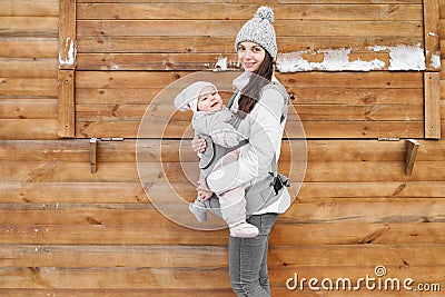 Little baby girl and her mother babywearing the ergo carrier in winter wooden background Stock Photo