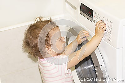 Little baby girl presses buttons on the washing machine Stock Photo