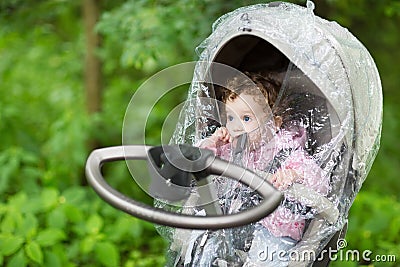 Little baby girl sitting in a stroller under a rain cover Stock Photo