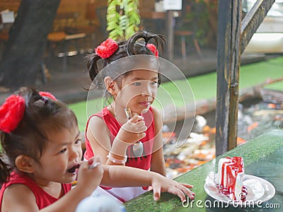 Little baby girls, sisters, enjoys eating a rainbow crepe cake with strawberry sauce on top at a restaurant Stock Photo